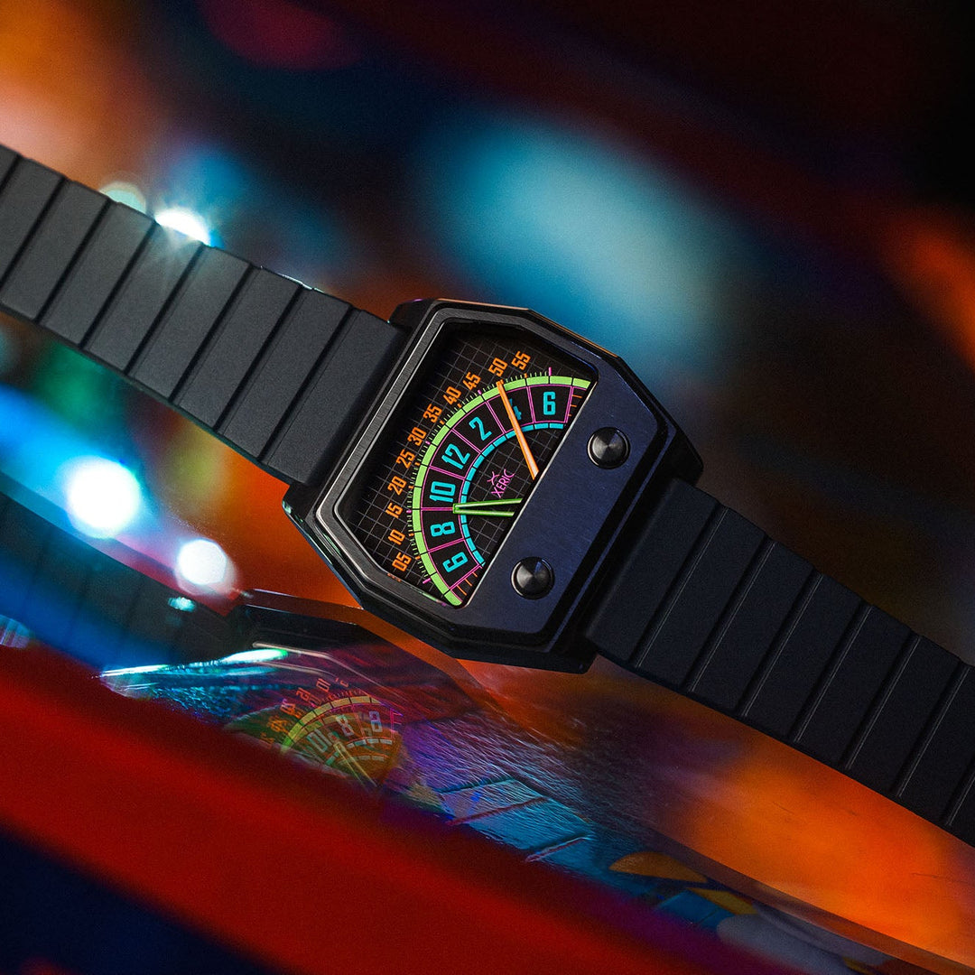 A black Casely watch with a bold, multi-colored retro dial and a matching black textured strap, shown in a dynamic close-up against a vibrant, blurred background of colorful lights.