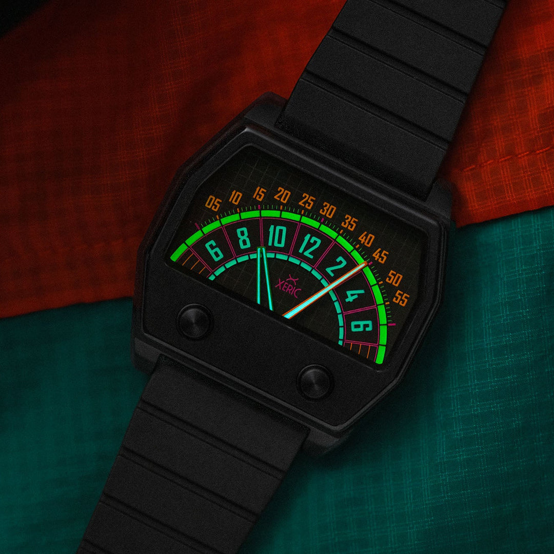 A black analog watch with a textured strap and a colorful dial featuring green, orange, and red markings, styled on a split red and teal fabric background.